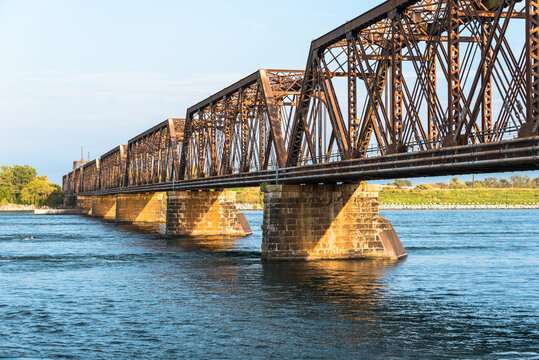 View of a rusty railroad bridge across a river at sunset
