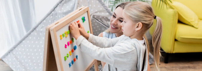 Woman looking at magnetic easel near kid at home, banner.