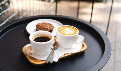 A cup of coffee and cup of cappuccino with chocolate chip cookies on the table in street cafe. Coffee break. Close-up.