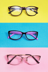 Group of trendy glasses for vision on a yellow, blue and pink background. Vertical. Stylish and beautiful glasses.