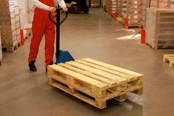 Worker moving wooden pallets with manual forklift in warehouse, closeup