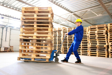 Worker moving wooden pallets with manual forklift in warehouse