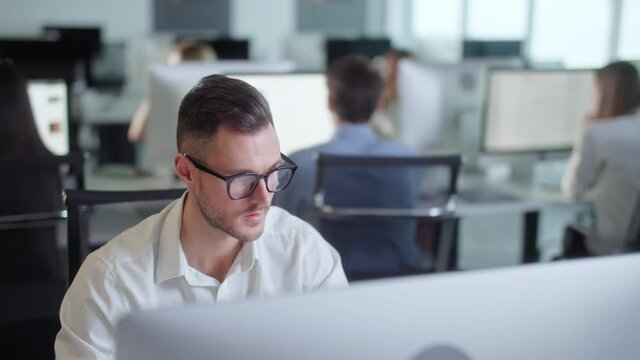 Serious Young Man Working on Decktop Computer While Working in Big Open Space Office. Portrait of Positive Business Man Looking at Computer Screen Indoors.