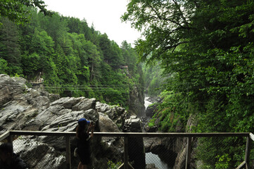 Woman wearing a hat walking on the bridge with the waterfalls running through the rock in the forest woods