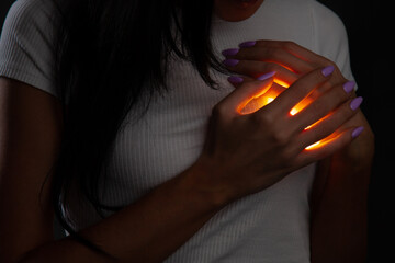 A woman covers a glowing burning heart in her chest with her hands. Front view  - Powered by Adobe
