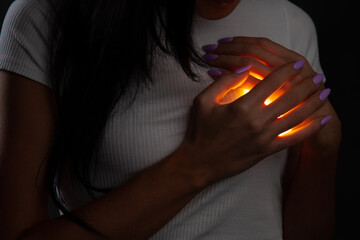 A woman covers a glowing burning heart in her chest with her hands. Front view  © Artem Rodionov