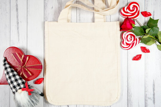 Tote bag product mockup. Valentine's Day farmhouse theme SVG craft product mockup styled with red roses, heart shaped gift, and buffalo plaid gnome against a white wood background. Flatlay.