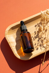 Amber glass dropper bottle with black lid on wooden backdrop for product presentation. Top view background with dry plants. Skincare cosmetic. Beauty concept for face body care