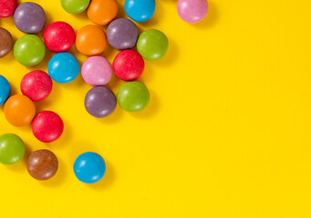 Colorful background of multicolored candy dragees. Round scattered sweets on a yellow bright background.