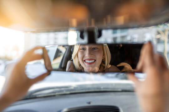 Woman hand adjusting rear view mirror of her car. Happy young woman driver looking adjusting rear view car mirror, making sure line is free visibility is good - Powered by Adobe