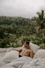 Young male traveller relaxing in a hotel in Bali, surrounded by nature, palm trees, rice fields and jungle views in Ubud, Indonesia, Asia