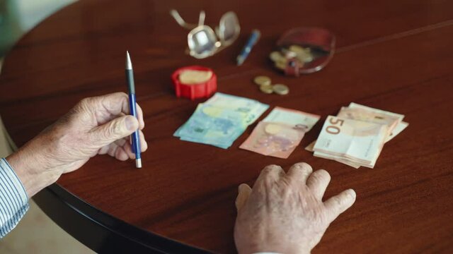Old businessman and entrepreneur sitting at the dest table in office and planning his budget counting monthly income and expenses, senior man saving business money for old age and investments, concept