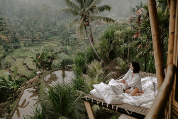 Young woman relaxing in a hotel in Bali, Indonesia, surrounded by jungle, palm trees and rice...