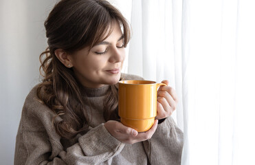 Attractive young woman with a cup of hot drink near the window.