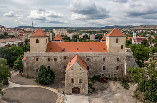 Aerial view of Varpalota Thury castle with newly renovated red orange roof, four rectangular towers in the middle of the former mining town with communist block houses in the background, modern vs old