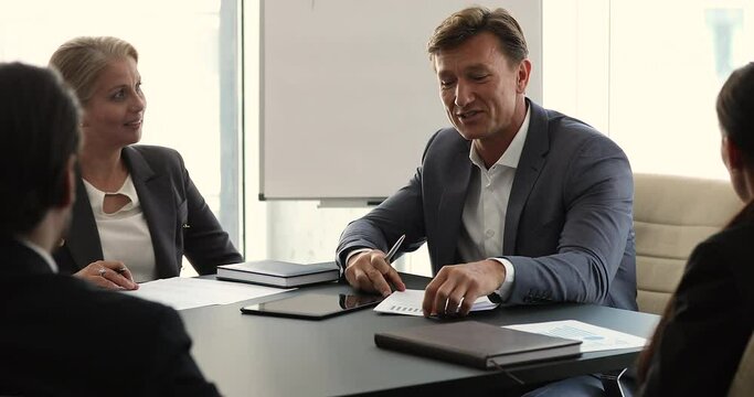 Businesspeople gather in board room take part in group meeting, focus on middle-aged company boss in suit holds briefing with employees, planning solve business together in office, negotiate concept