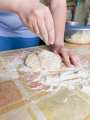 Hand sprinkles flour on piece of dough on table