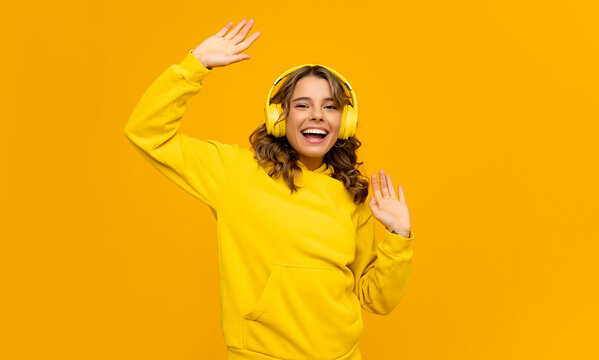 smiling attractive woman listening to music in headphones on yellow background