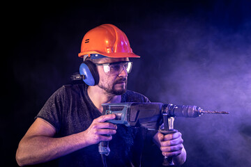 Fototapeta premium A young man in overalls protective helmet hard hat hold electric drill.