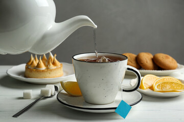 Pouring hot water into cup with tea bag at white wooden table
