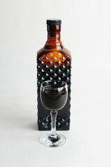 Coffee liqueur in dark glass bottle behind a filled shot glass. White background, isolated