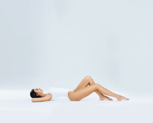 Obraz premium Young, fit and beautiful brunette woman in white swimsuit posing in studio. Concept of fitness, dieting and skin care.