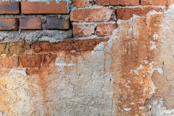 Old exterior brick wall with damaged falling plaster close up