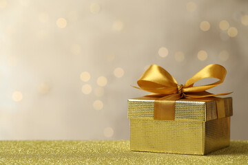Beautiful gift box on golden table against blurred festive lights, space for text