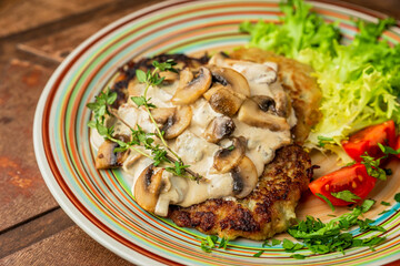 A close-up of potato pancakes with mushroom cream sauce, lettuce, cherry tomatos and thyme, wooden table