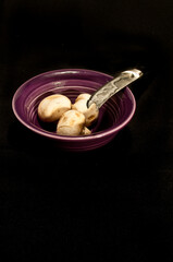 top view, medium distance of a purple, ceramic,  bowl with three mushrooms and a knife blade