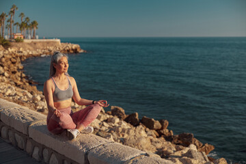 Sporty active woman in sports clothes sitting by the beautiful seashore and taining on sunny day