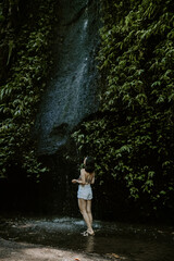 A young female traveller exploring waterfall in Bali. Nature, green lush tropical landscapes, water, woman