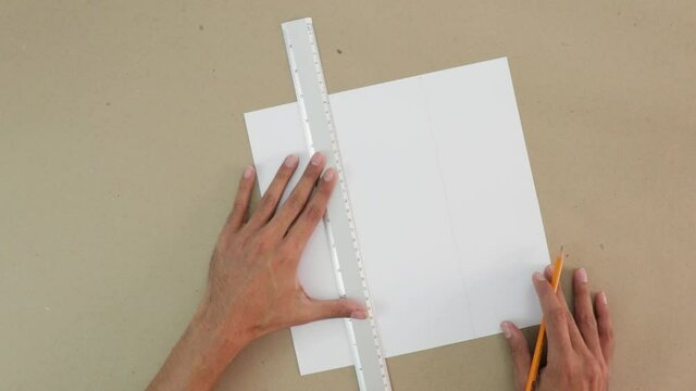Trace a 3x3 grid on white cardboard. Craft paper background. Ruler and pencil are used. Brown hands. School activity. 