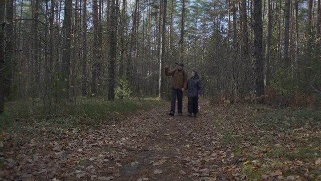 Adult man with son and small pet dog walking on forest footpath at autumn season. Togetherness and friendship conception.