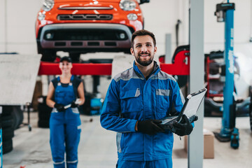 Fototapeta Male and female mechanics working together in large modern car repair service. obraz