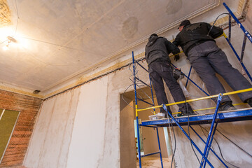 Two workers is installing the electrical wires on the wall that is the part of internal wiring in apartment that is under construction, remodeling, renovation, extension, restoration  