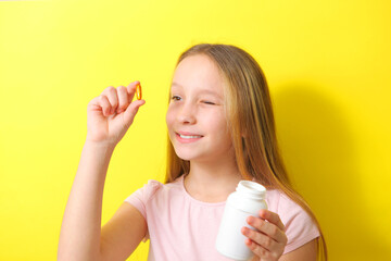 A teenage girl holds an omega 3 capsule in her hands on a colored background. 