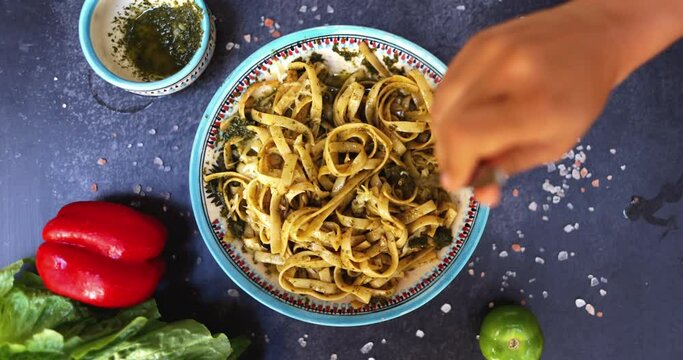 Hand with fork twisting delicious noodles on plate above black surface