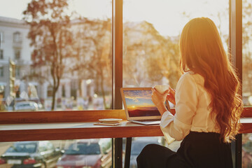 Unrecognizable woman at cafe looking at window, working remotely using laptop, person take a break during online work