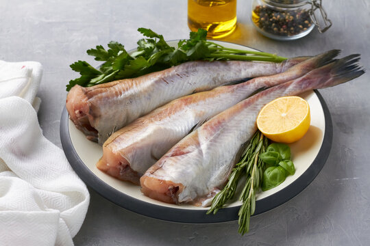 raw pollock fish on plate lemon parsley rosemary grey background