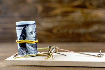 Dollars in a mousetrap with a hundred dollar bill on a wooden background with a copy space