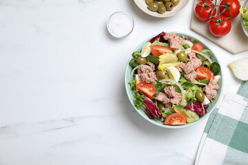 Bowl of delicious salad with canned tuna and vegetables on white marble table, flat lay. Space for text