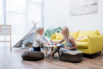 Side view of smiling mother and daughter drawing near couch and teepee at home.