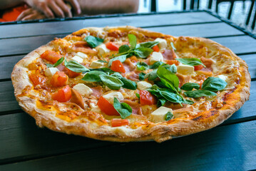 Fresh pizza with feta cheese, fresh basil and tomatoes on table