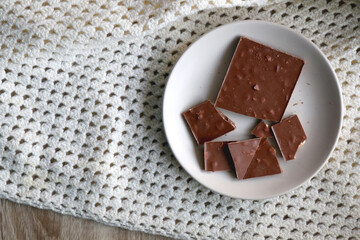 Almond and hazelnut chocolate bar on a plate and soft knited blanket. Top view. 