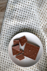 Almond and hazelnut chocolate bar on a plate and soft knited blanket. Top view. 