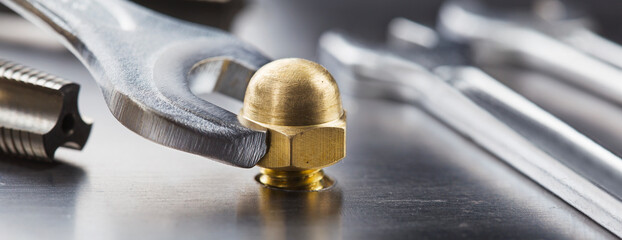 Wrench tightens brass cap nut in steel billet. Spanner, bolt, screw and nuts.