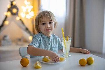 Cute toddler child, blond boy, licking lemons at home and drinking lemonade