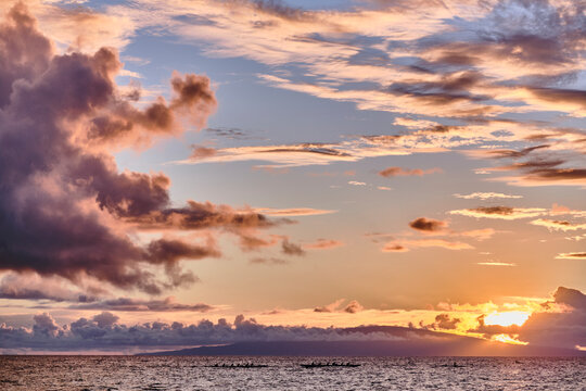 Two groups of paddlers travel in traditional canoes during sunset
