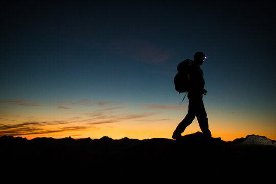 Backpacker hiking ridge at night via headlamp.